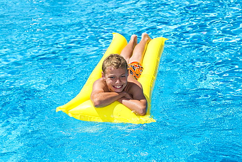 Boy, 12 years, lying on a lilo in a swimming pool