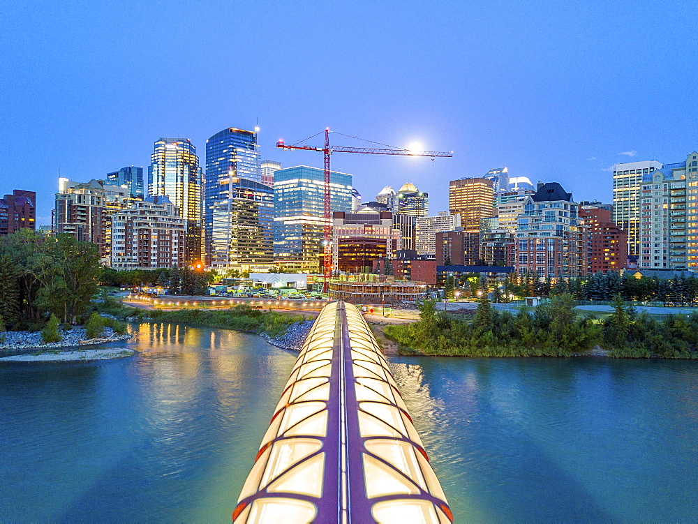 Calgary downtown at dusk with iluminated Peace Bridge and full moon, Alberta, Canada, North America (Drone)