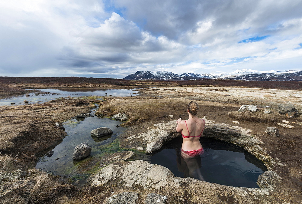 Young woman in hot spring looking towards mountains, Eyjar og Miklaholt, Western Region, Iceland, Europe