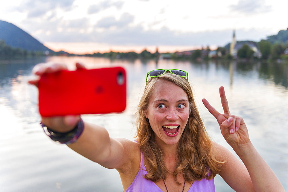 Young woman taking selfie, laughing and making peace sign, Schliersee, Upper Bavaria, Bavaria, Germany, Europe