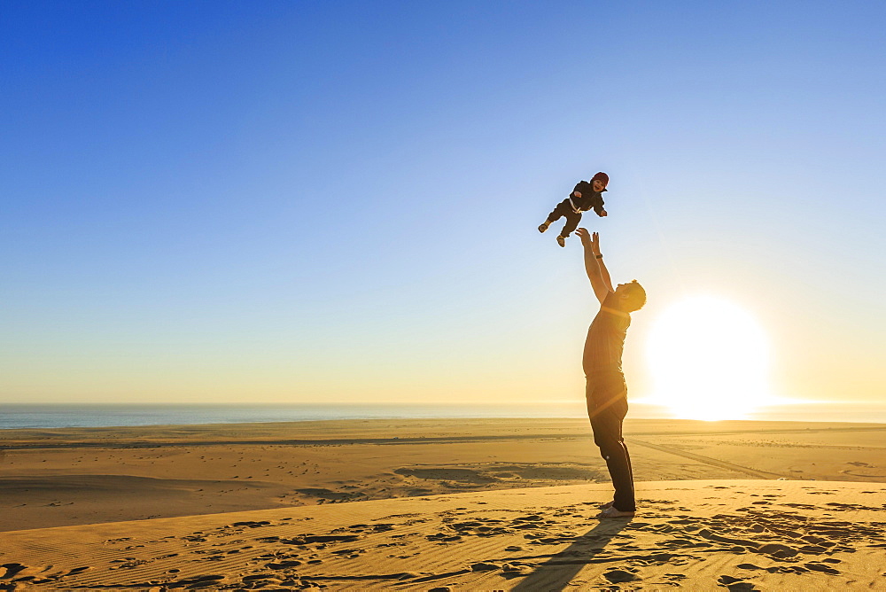 Father throws his little laughing son in the air, sandy beach, Langstrand, Namib Desert, Swakopmund, Erongo Region, Namibia, Africa