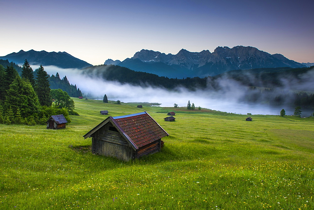 Small cabin on mountain meadow at forest edge, Geroldsee in the background Karwendel Mountains at sunrise, Kaltenbrunn, Upper Bavaria, Germany, Europe