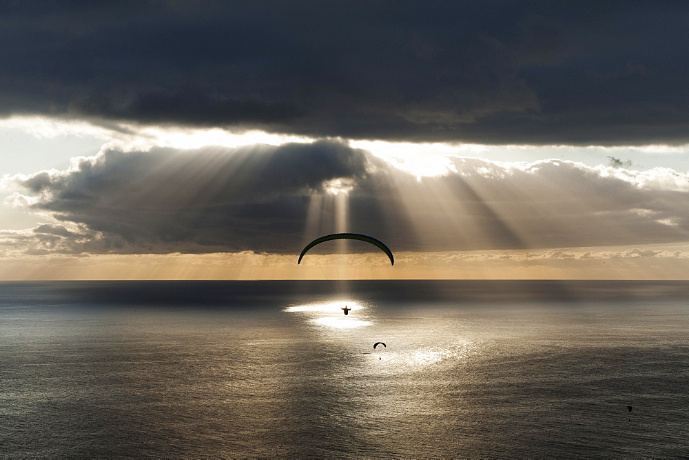 Sun shines behind dark clouds with paraglider over the Atlantic, Puerto Naos, Canary Island of La Palma, Spain, Europe