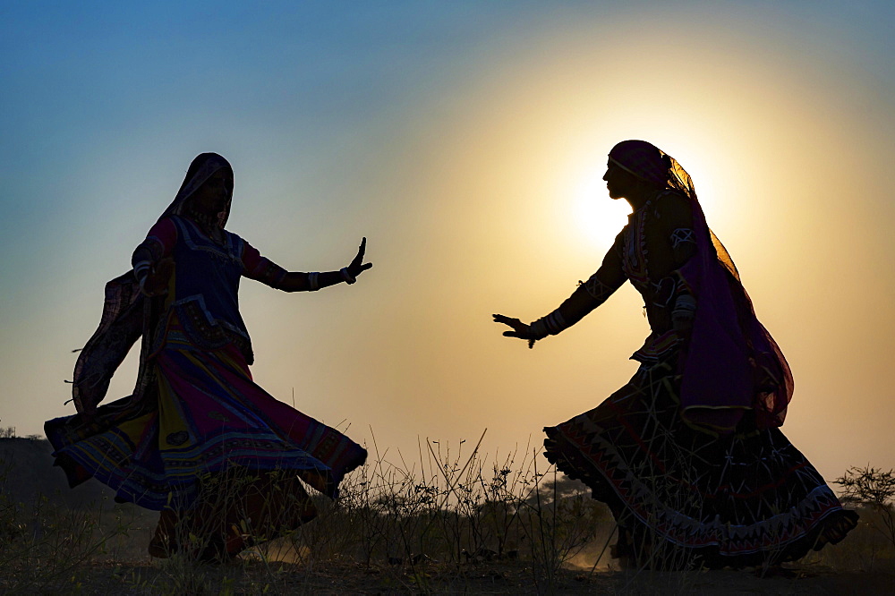 Two young women in dresses dancing in front of the setting sun, Pushkar Camel Fair, Pushkar, Rajasthan, India, Asia