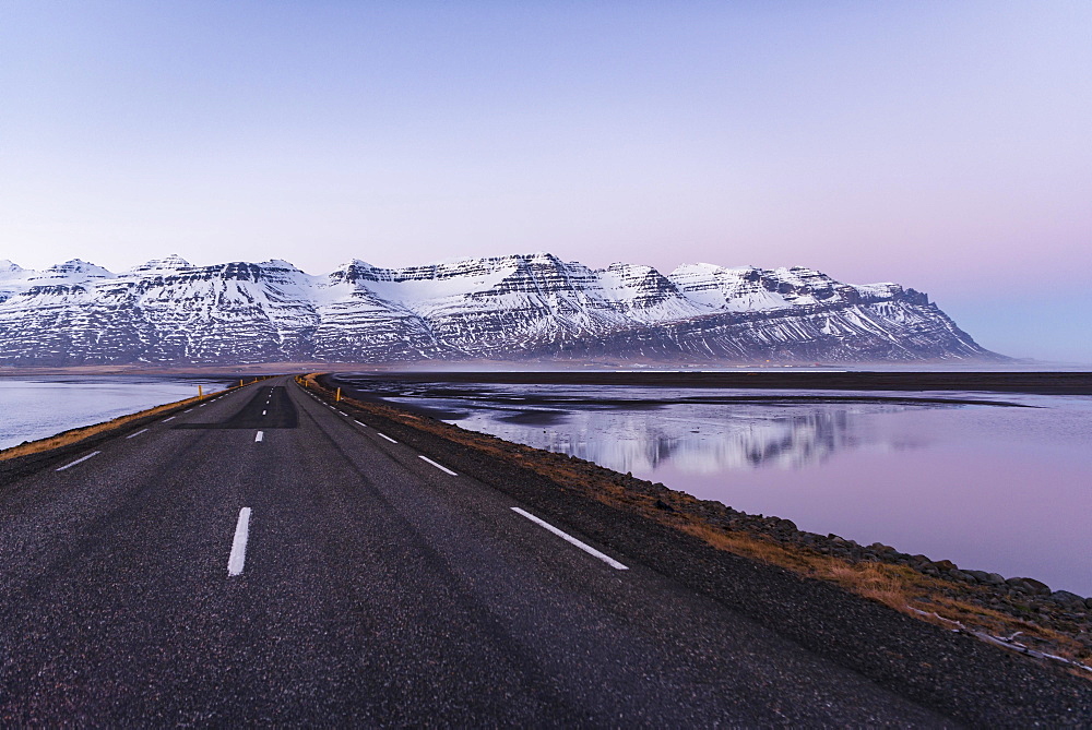 Ring road, country road by the sea, rugged volcanic landscape, mountains with snow, sunset, Iceland, Europe