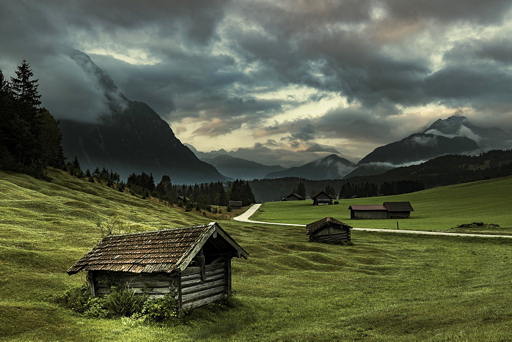 Small huts on mountain meadow with dramatic cloud sky and Wetterstein mountains in the background, Mittenwald, Bavaria, Germany, Europe