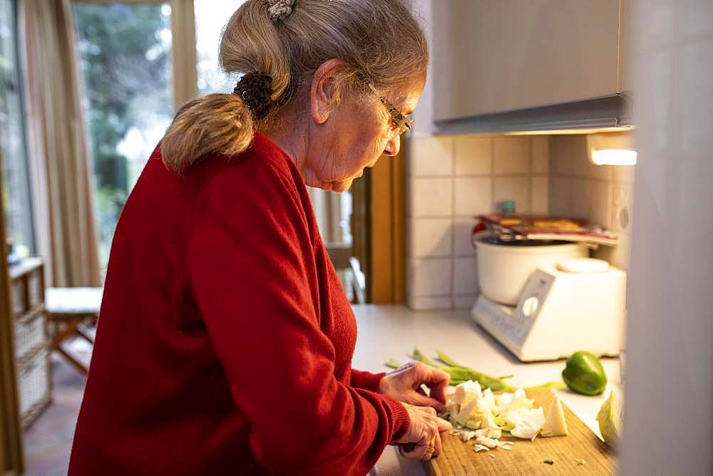 Senior cuts vegetables in the kitchen, Germany, Europe