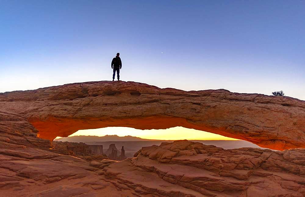 Young man standing on rock arch, Mesa Arch, sunrise, Grand View Point Road, Island in the Sky, Canyonlands National Park, Moab, Utah, USA, North America