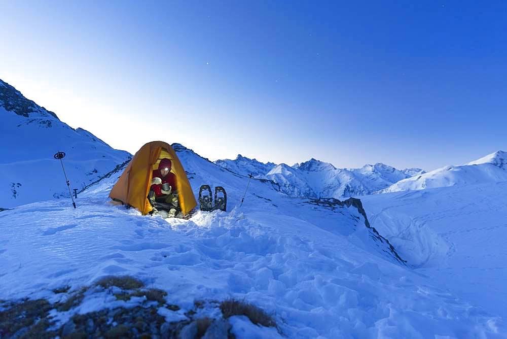 Snowshoe hiker in tent eating in the snow on the Maedelejoch, near Kemptner Huette, Allgaeuer Alps, Tyrol, Austria, Europe