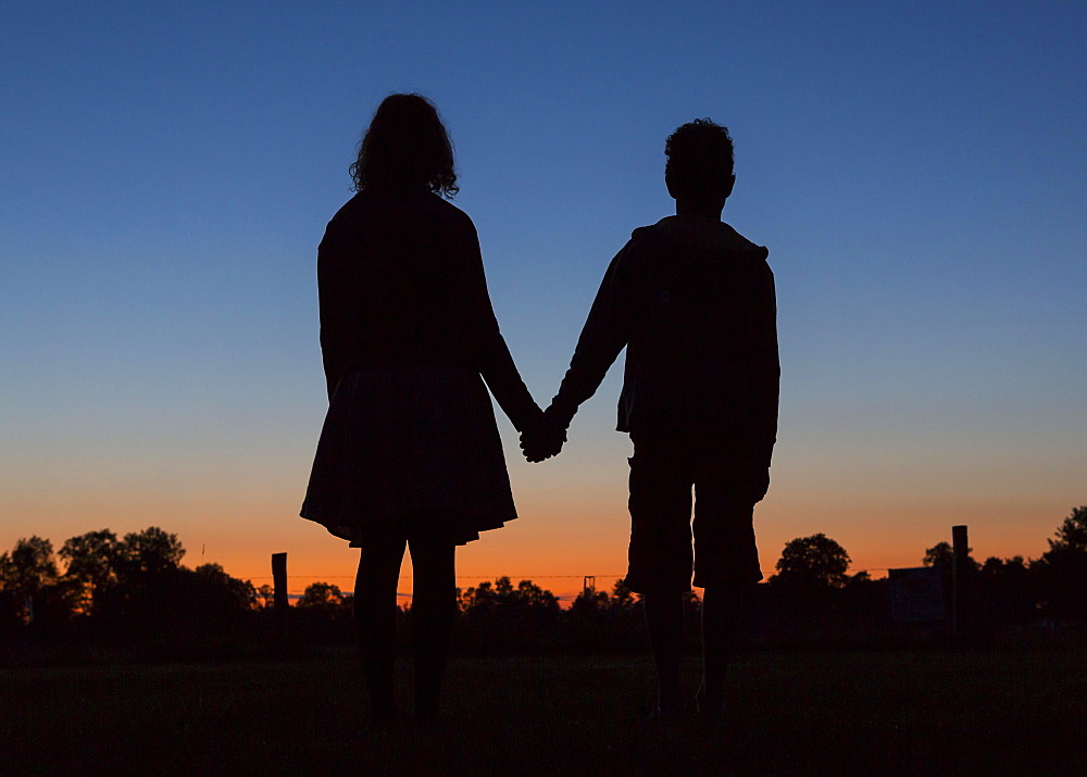 Silhouette in front of evening sky, two children holding hands, Germany, Europe