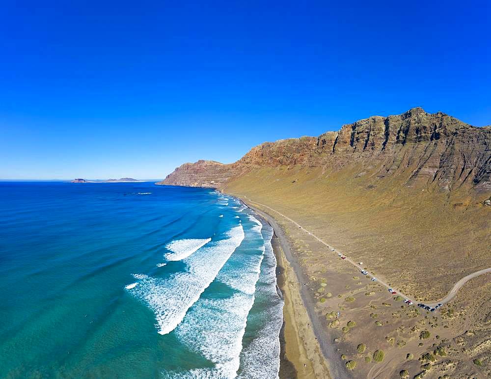 View on beach Playa Famara with mountain range Risco de Famara, at Caleta de Famara, behind island La Graciosa, drone shot, Lanzarote, Canary Islands, Spain, Europe