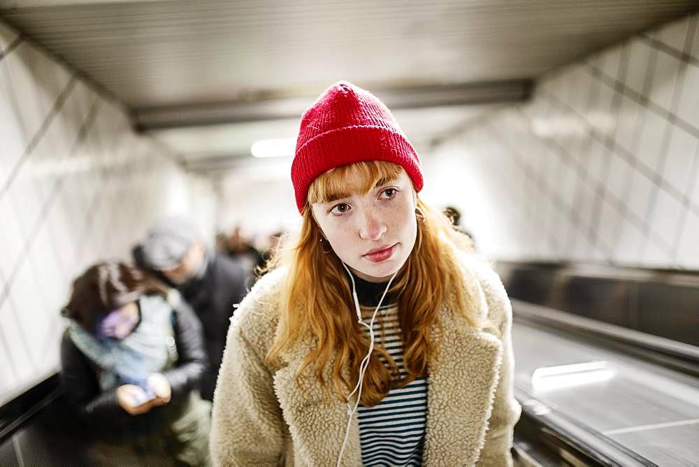 Girl, teenager, with red beanie and headphones in ear on escalator of a subway station, Cologne, North Rhine-Westphalia, Germany, Europe