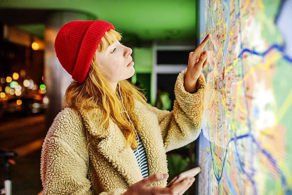 Girl, teenager, with smartphone in her hand standing at night in the city in front of city map, Cologne, North Rhine-Westphalia, Germany, Europe