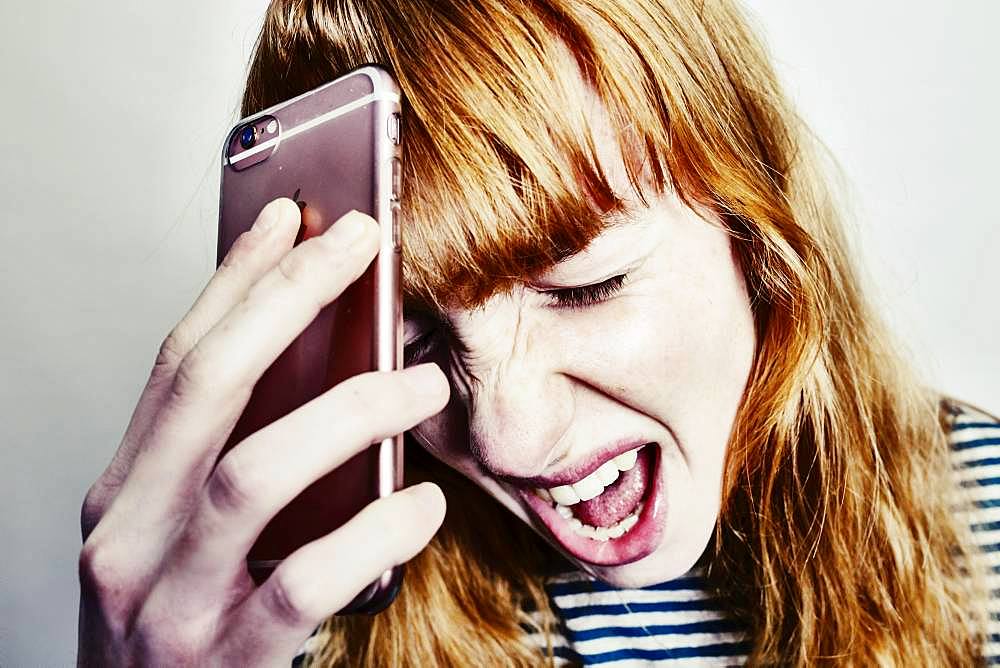 Girl, teenager, red-haired, holding her head in despair screaming smartphone, studio shot, Germany, Europe