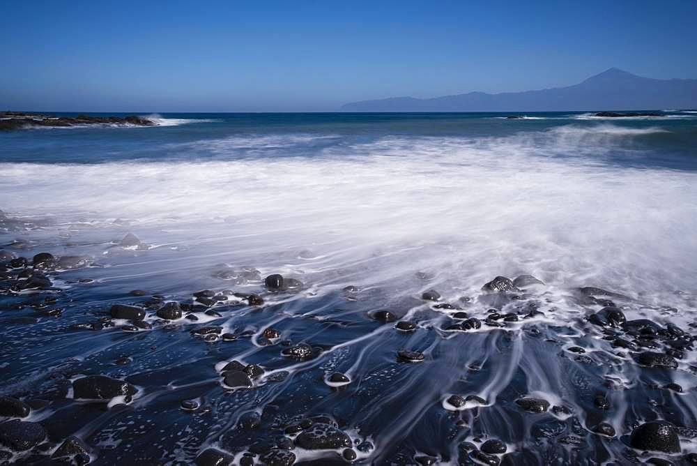 Black pebble beach with wave hem, time exposure, view to Teide on Tenerife, Playa de Caleta, La Gomera, Canary Islands, Spain, Europe