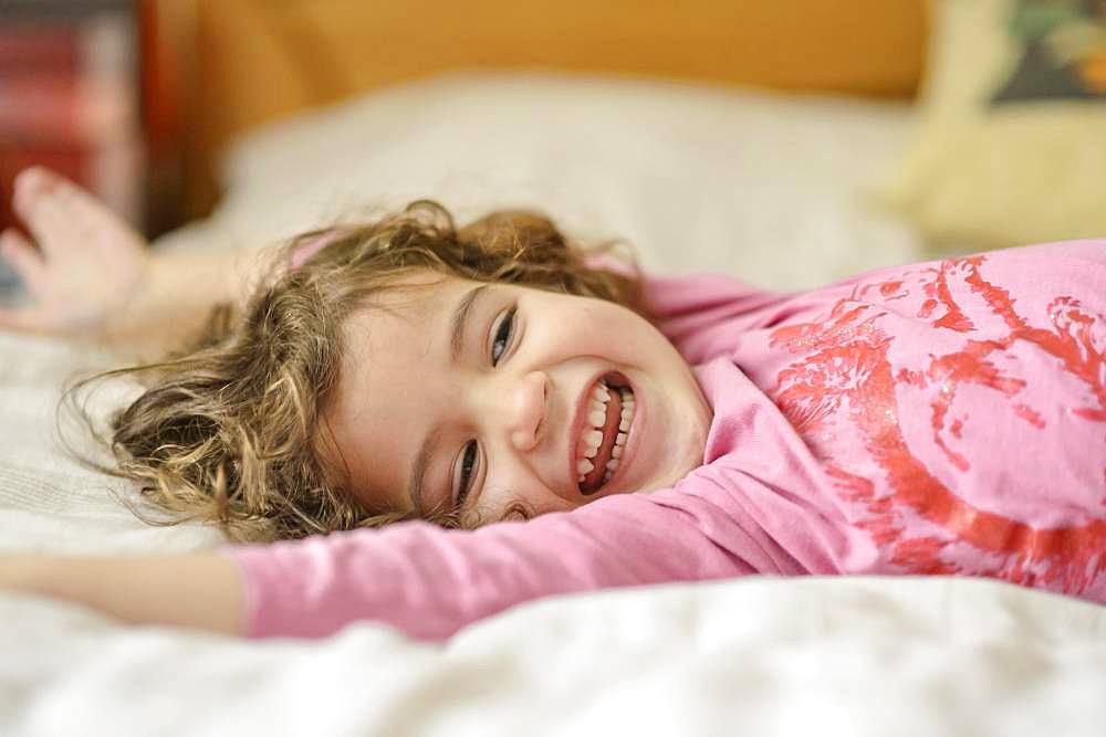 Girl, 3 years old, portrait, lies relaxed and laughing in bed, Germany, Europe