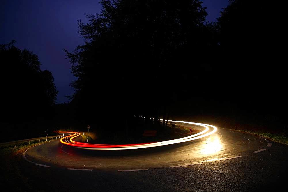 Car driving on winding country road at night, white and red light tracksHaarnadelkurve, Reinhardswald, Hesse, Germany, Europe