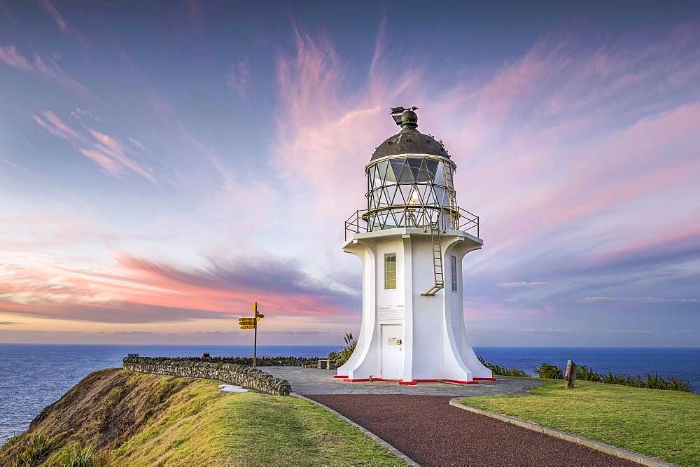 Lighthouse with signpost at Cape Reinga at sunset with pink clouds, Far North District, Northland, North Island, New Zealand, Oceania