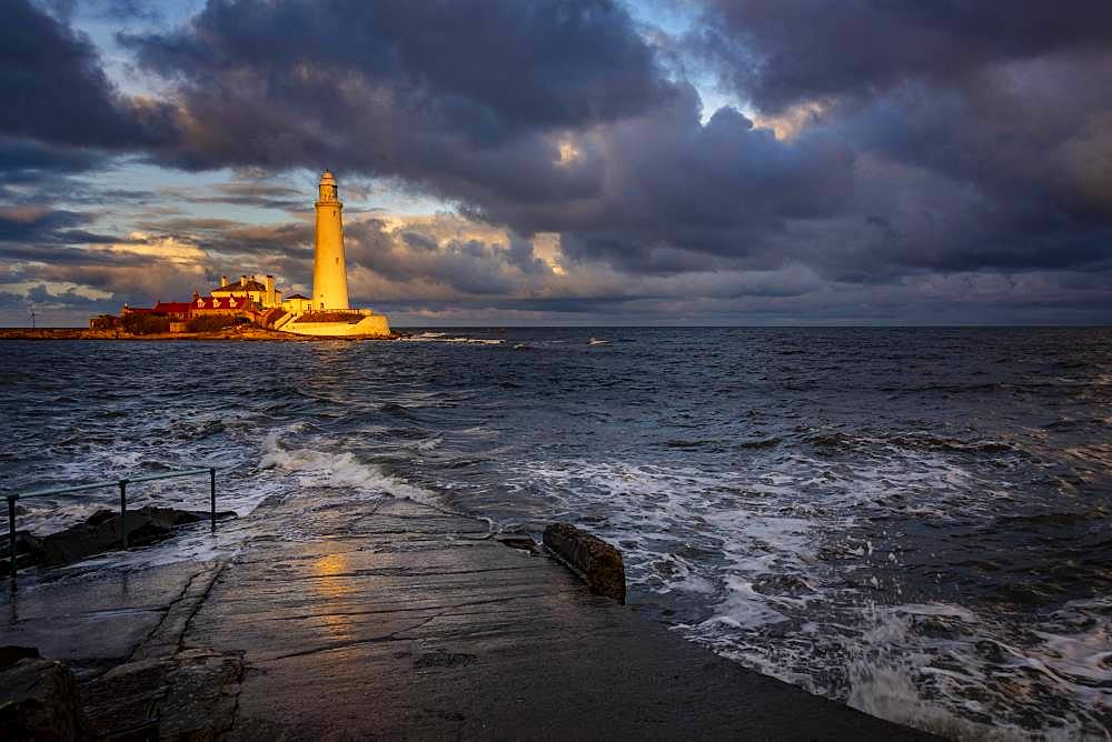 Lighthouse, St. Mary's Lighthouse with washed over road at high tide with dramatic clouds at sunset, Coast of Tyne, Northumberland, Great Britain