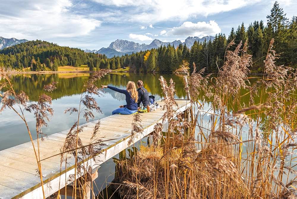 Two young women sitting at a jetty having a snack, Lake Geroldsee, Mittenwald, Karwendel, Bavaria, Germany, Europe