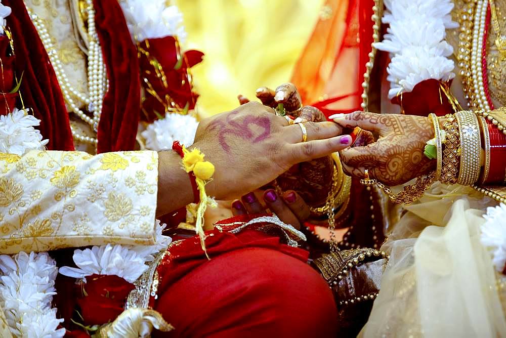 Bride with bridal jewelry and henna decoration on her hand attaches ring to the grooms finger at traditional religious ceremony at a Hindu wedding, Mauritius, Africa