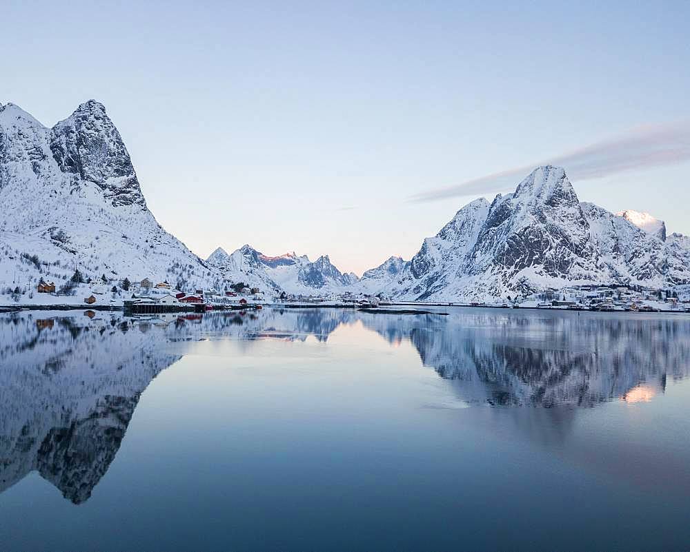 Snow-covered mountains reflected in fjord, sunrise, drone shot, Reine, Lofoten, Norway, Europe