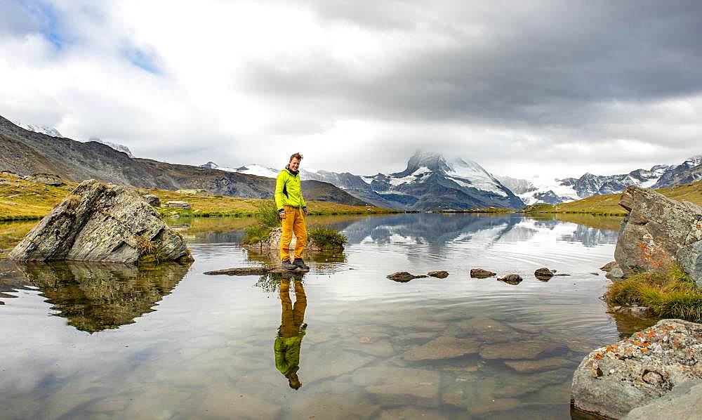 Hiker walks over stones in the water, Lake Stellisee, cloudy Matterhorn, Valais, Switzerland, Europe