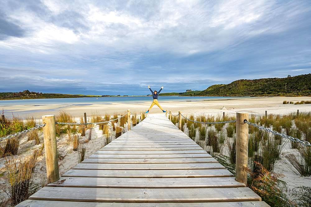 Young man jumps, boardwalk to the beach, Taharoa Lake, Northland, North Island, New Zealand, Oceania