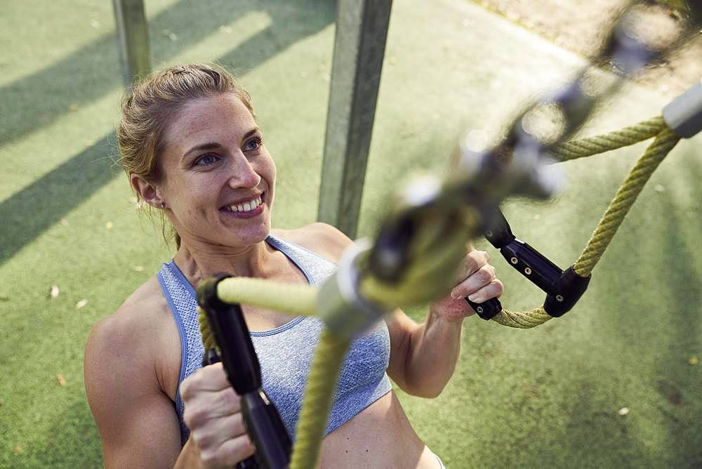 Sporty young woman doing fitness training on the rings, outdoor sports, sporty, Olympiapark, Munich, Germany, Europe