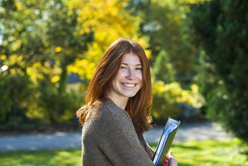 Young smiling red-haired woman, student, pupil holds folder, Bavaria, Germany, Europe