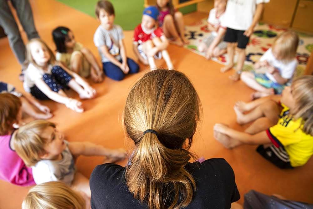 Educator sits with children in the kindergarten in a circle on the floor, Cologne, North Rhine-Westphalia, Germany, Europe