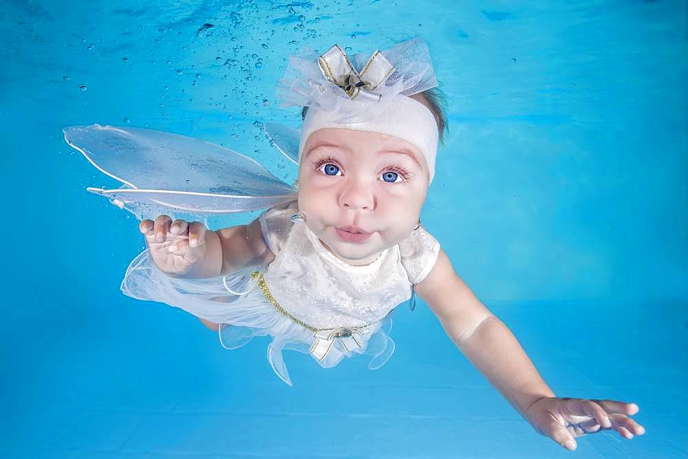 Little girl in fairy costume dives underwater in a swimming pool