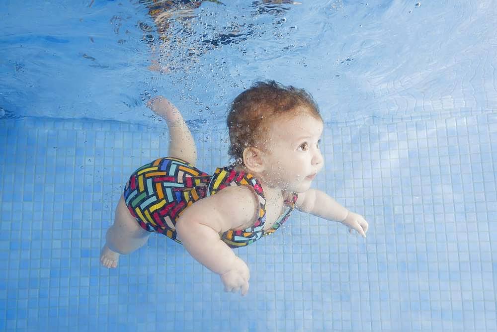 Little baby in a swimsuit learning to swim underwater in a swimming pool, Ukraine, Europe