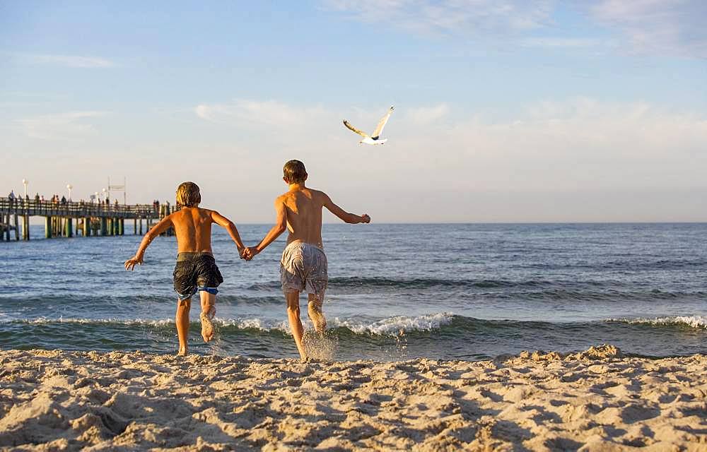 Two young people run into the water at the Baltic Sea beach, Kuehlungsborn, Mecklenburg-Western Pomerania, Germany, Europe