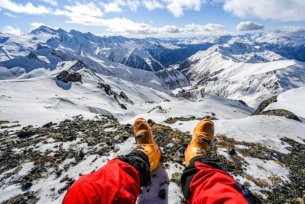 View from the summit of the Geierspitze, legs with ski boots in front of a snow-covered mountain panorama, Wattentaler Lizum, Tuxer Alps, Tyrol, Austria, Europe