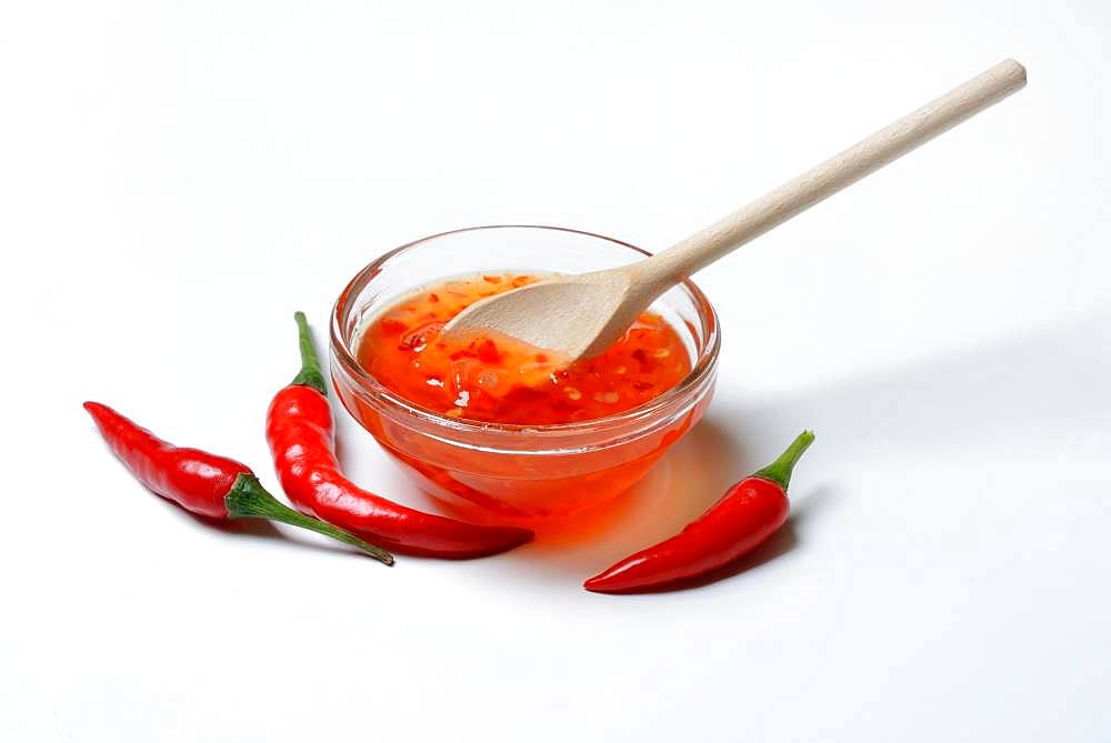 Chilli sauce in small bowl with cooking spoon and chilli peppers, Germany, Europe