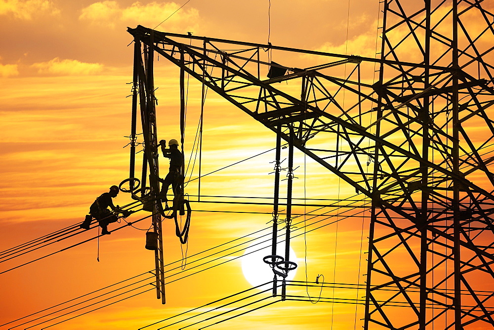 High voltage fitters working on the high voltage pylon at sunset, Baden-Wuerttemberg, Germany, Europe