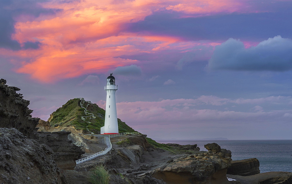 Lighthouse in the evening light under a pink cloudy sky on the cliffs at Castlepoint, Lavafels, Masterton, Wellington, New Zealand, Oceania