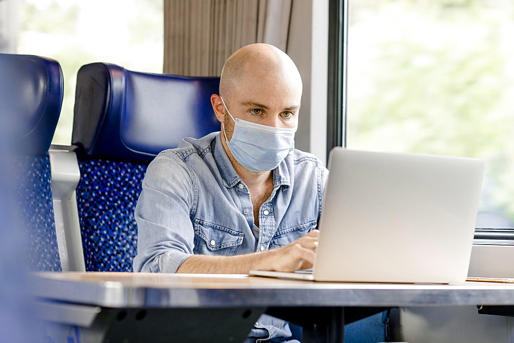 Train ride with mouth protection mask, man working on laptop, Germany, Europe