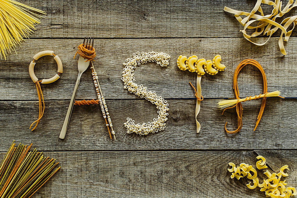 Word pasta from different noodles on wooden table, pasta