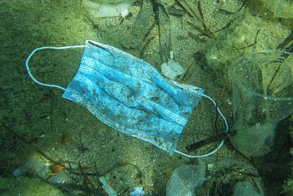 Discarded used medical face mask lies on the seabed together with other plastic waste, Becici, Budva region, Montenegro, Europe