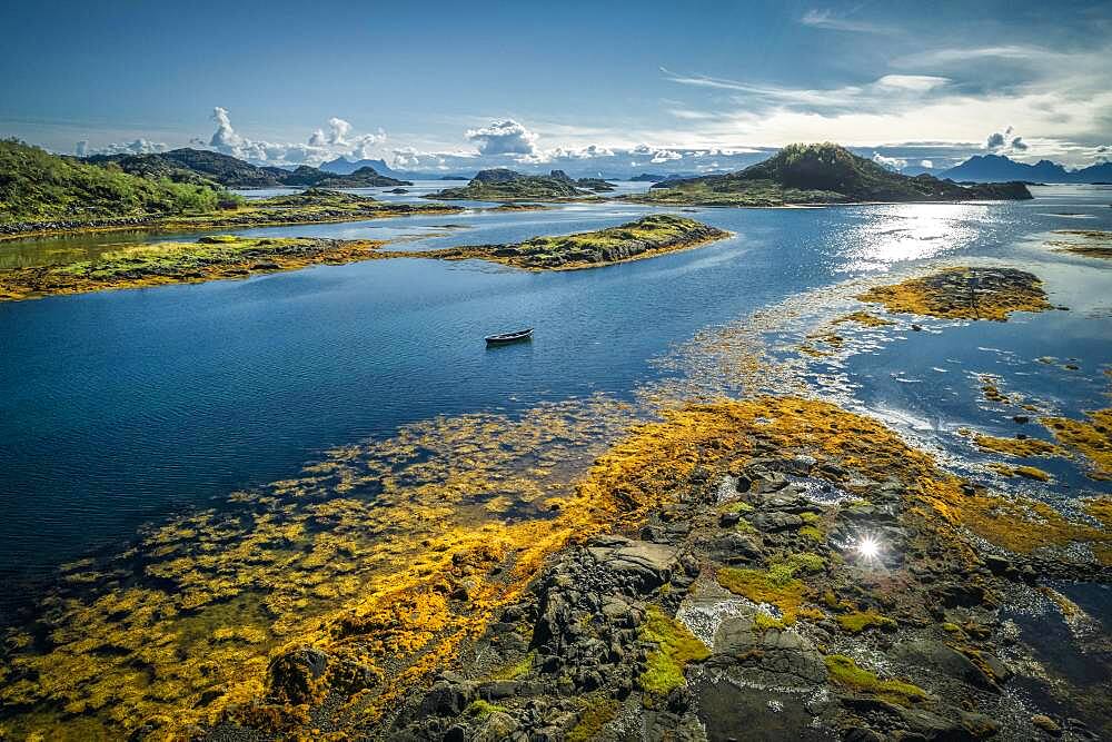 Fjord landscape with small rock islands at low tide with yellow seaweed, small wooden boat between archipelagos in the sea, Lodingen, Nordland, Lofoten, Norway, Europe