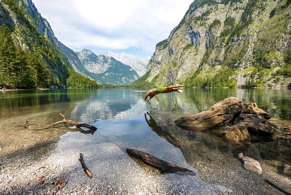 Young man jumps into lake, bathes in mountain lake, mountains are reflected in Obersee, behind Watzmann, salet at Koenigssee, Berchtesgaden National Park, Berchtesgadener Land, Upper Bavaria, Bavaria, Germany, Europe