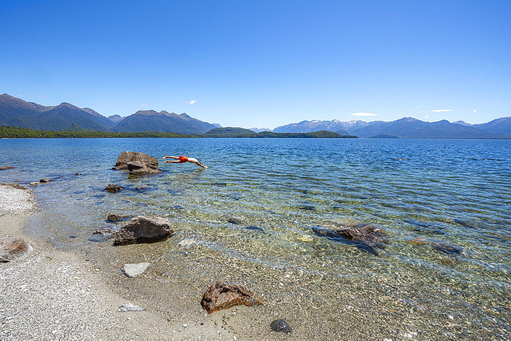 Young man jumps from stone into water, Beach Frasers Beach, Lake Manapouri, Manapouri, South Island, New Zealand, Oceania