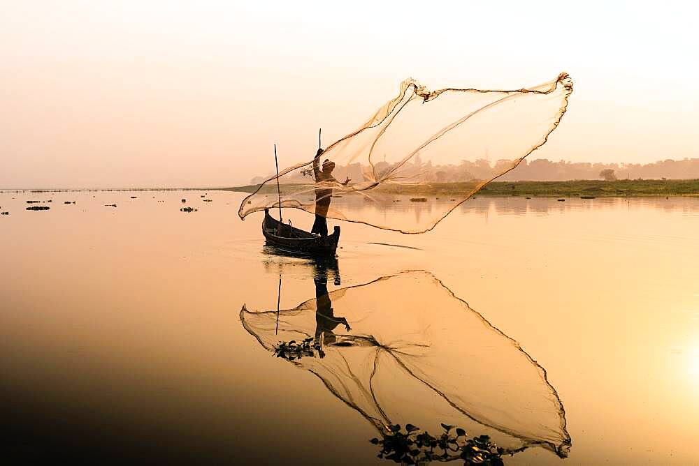 Fisherman with boat on Taung Tha Man Lake casts a fishing net for sunrise, reflection in the water, Thaung Tha Man Lake, Mandalay, Myanmar, Asia