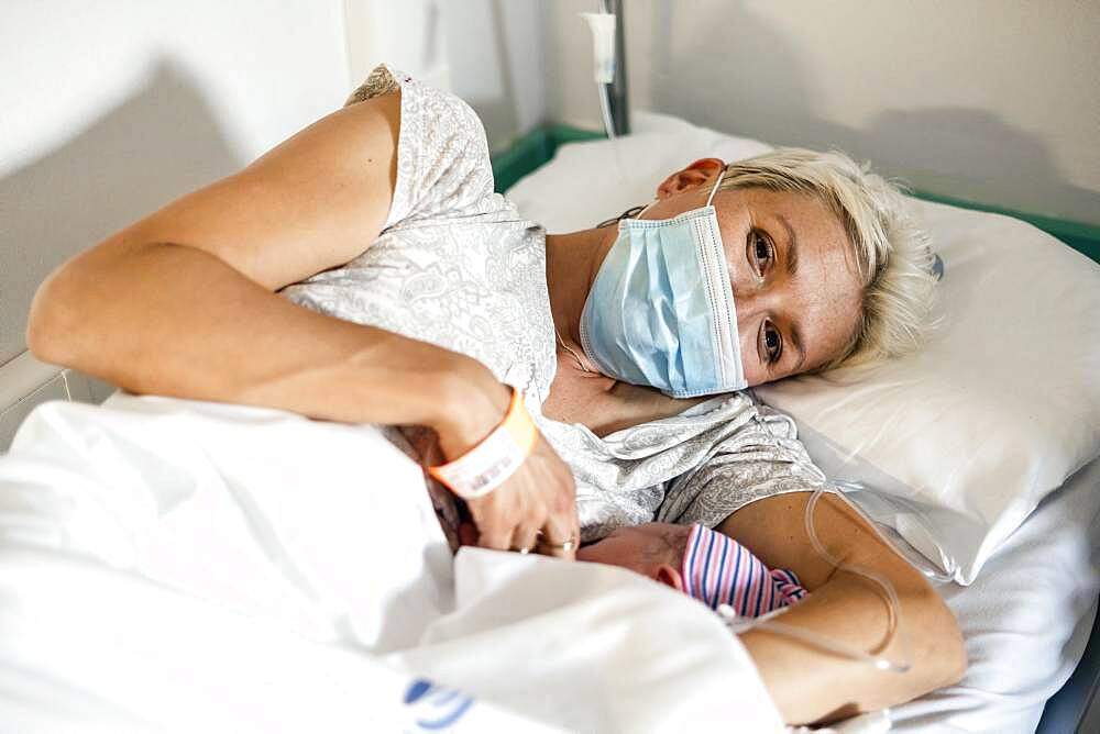 Mother wearing a respirator breastfeeds her newborn baby in hospital