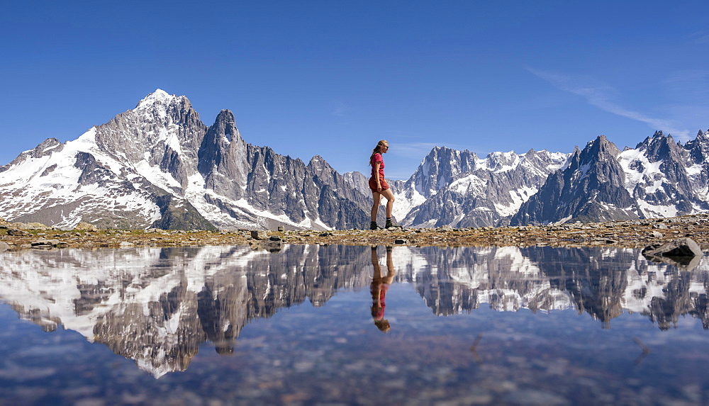 Young woman walking in front of mountain panorama, reflection in Lac Blanc, mountain peaks, Grandes Jorasses and Mont Blanc massif, Chamonix-Mont-Blanc, Haute-Savoie, France, Europe