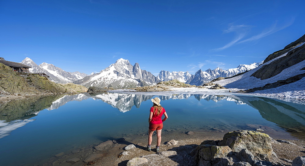 Young woman in front of mountain panorama, reflection in Lac Blanc, mountain peaks, Grandes Jorasses and Mont Blanc massif, Chamonix-Mont-Blanc, Haute-Savoie, France, Europe