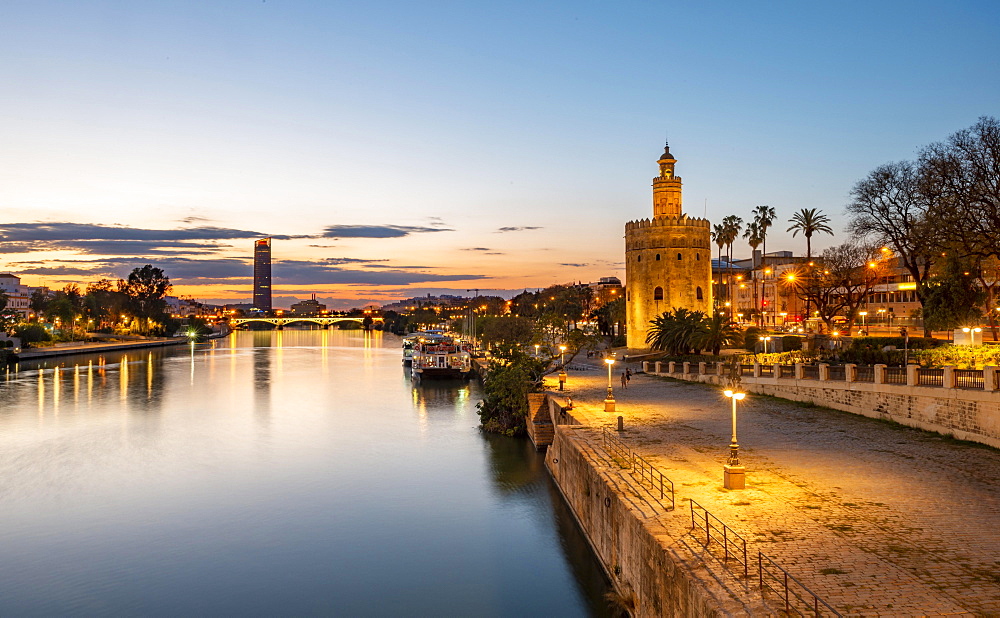 View over the river Rio Guadalquivir with Torre del Oro, promenade and Puente de Triana, in the back Torre Sevilla, sunset, blue hour, Sevilla, Andalusia, Spain, Europe