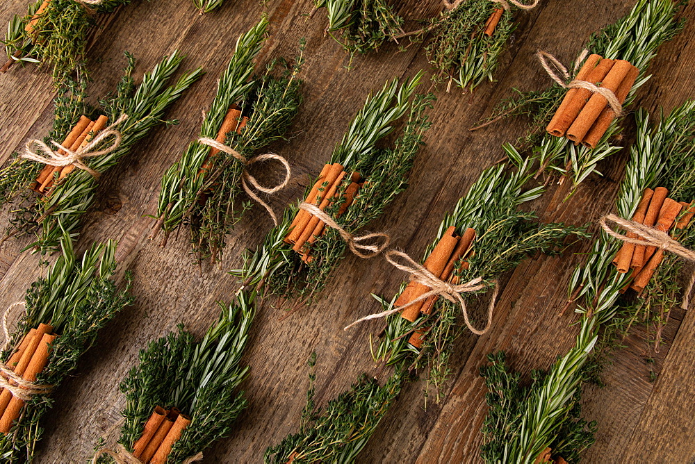 Cinnamon sticks tied together with rosemary and thyme, several bunches of herbs next to each other, on wooden underground